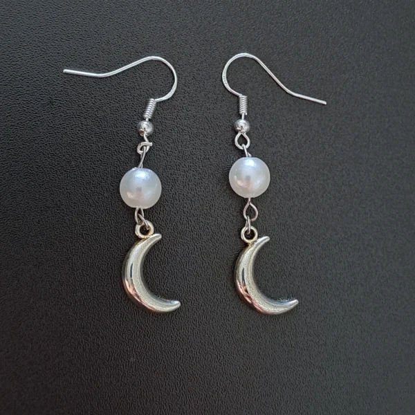 A pair of earrings featuring a round acrylic pearl in white and silver crescent moon charms