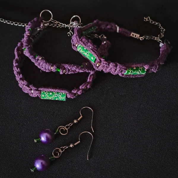 Jewelry set consisting of three braided bracelets (purple suede cords with green floral beads), and a pair of handmade earrings featuring round purple pearls, small green glass beads and silver swirls.