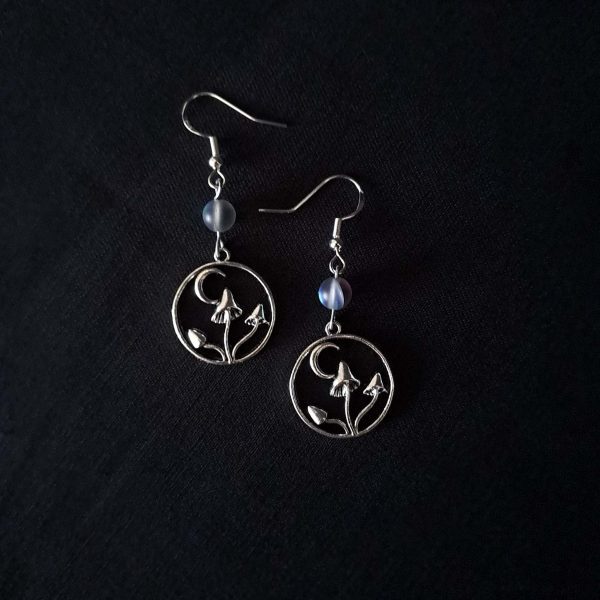Nocturnal mushroom earrings. A stainless steel charm contains three rising mushrooms, and a half moon. Above the charms lays a translucent iridescent grey-blue bead, reminiscent of moonstone. Very witchy and gothic vibes