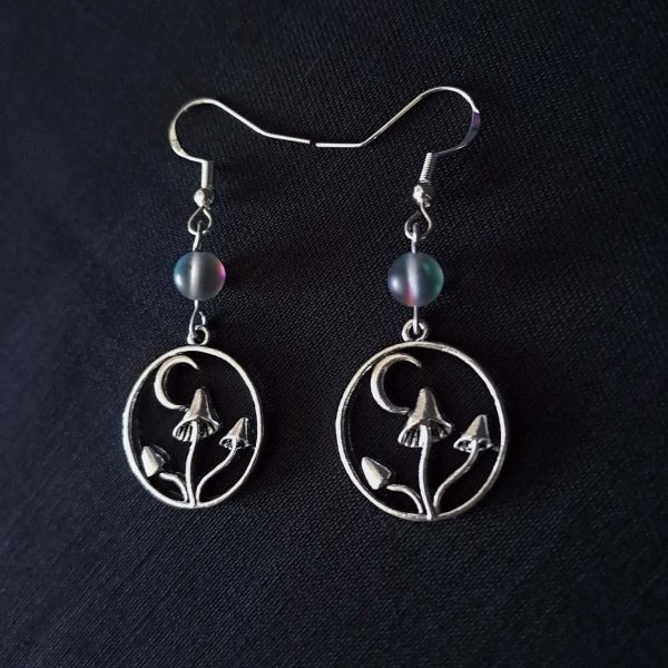 Nocturnal mushroom earrings. A stainless steel charm contains three rising mushrooms, and a half moon. Above the charms lays a translucent iridescent grey-blue bead, reminiscent of moonstone. Very witchy and gothic vibes