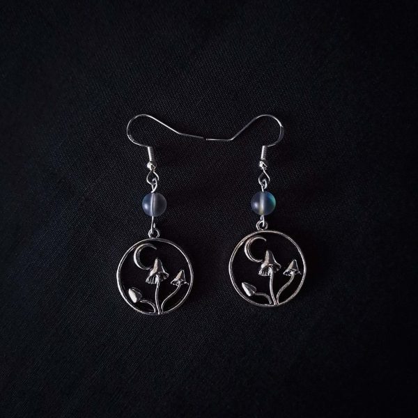Nocturnal mushroom earrings. A stainless steel charm contains three rising mushrooms, and a half moon. Above the charms lays a translucent iridescent grey-blue bead, reminiscent of moonstone. Very witchy and gothic vibes