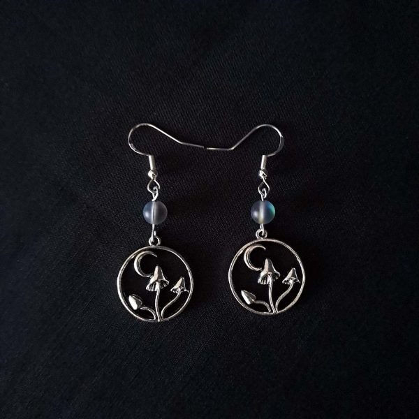 Nocturnal mushroom earrings. A stainless steel charm contains three rising mushrooms, and a half moon. Above the charms lays a translucent iridescent grey-blue bead, reminiscent of moonstone. Very witchy and gothic vibes
