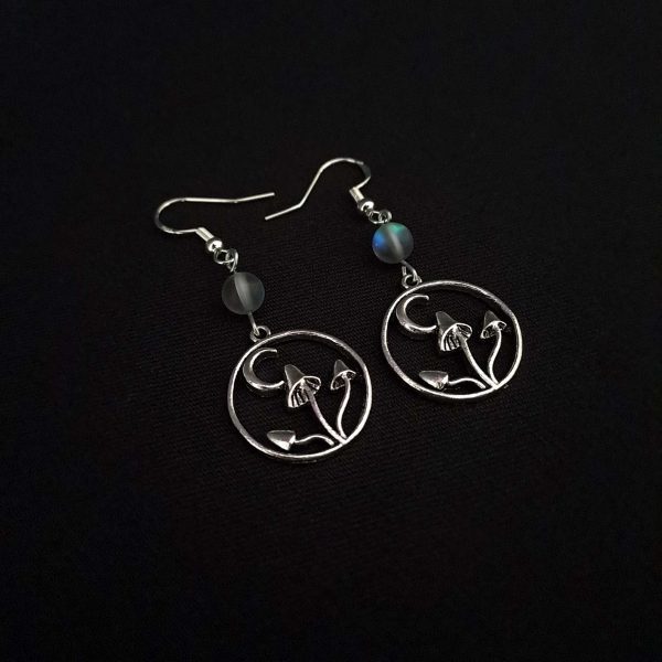 Nocturnal mushroom earrings. A stainless steel charm contains three rising mushrooms, and a half moon. Above the charms lays a translucent iridescent grey-blue bead, reminiscent of moonstone. Very witchy and gothic vibes