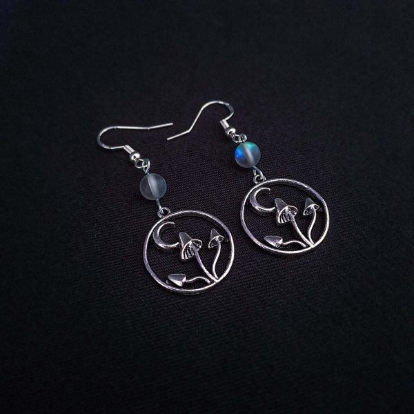 Nocturnal mushroom earrings. A stainless steel charm contains three rising mushrooms, and a half moon. Above the charms lays a translucent iridescent grey-blue bead, reminiscent of moonstone. Very witchy and gothic vibes