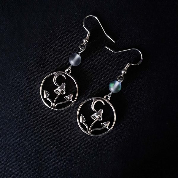 Nocturnal mushroom earrings. A stainless steel charm contains three rising mushrooms, and a half moon. Above the charms lays a translucent iridescent grey-blue bead, reminiscent of moonstone. Very witchy and gothic vibes