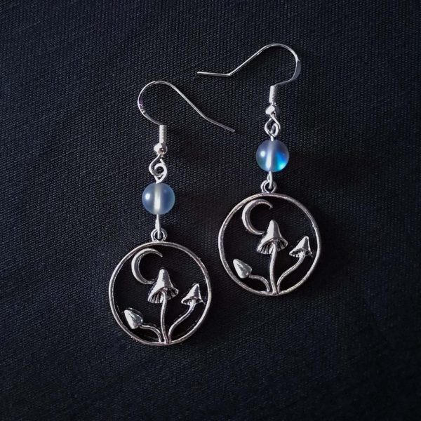 Nocturnal mushroom earrings. A stainless steel charm contains three rising mushrooms, and a half moon. Above the charms lays a translucent iridescent grey-blue bead, reminiscent of moonstone. Very witchy and gothic vibes