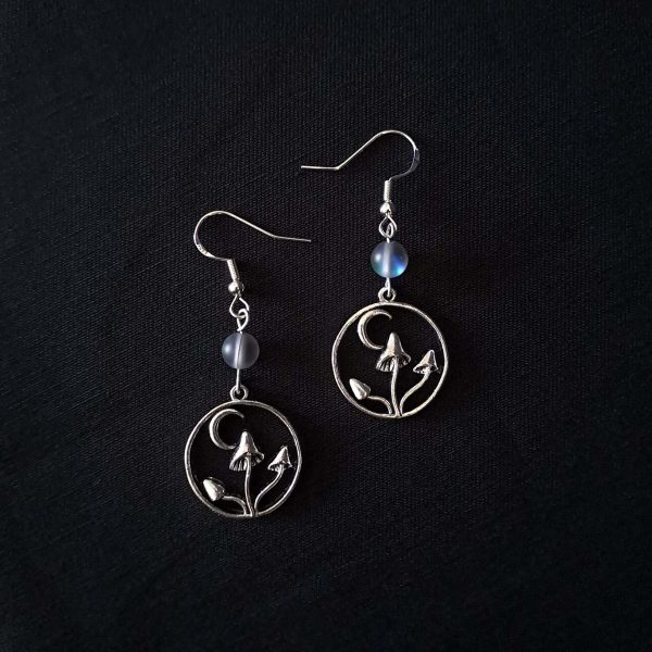 Nocturnal mushroom earrings. A stainless steel charm contains three rising mushrooms, and a half moon. Above the charms lays a translucent iridescent grey-blue bead, reminiscent of moonstone. Very witchy and gothic vibes
