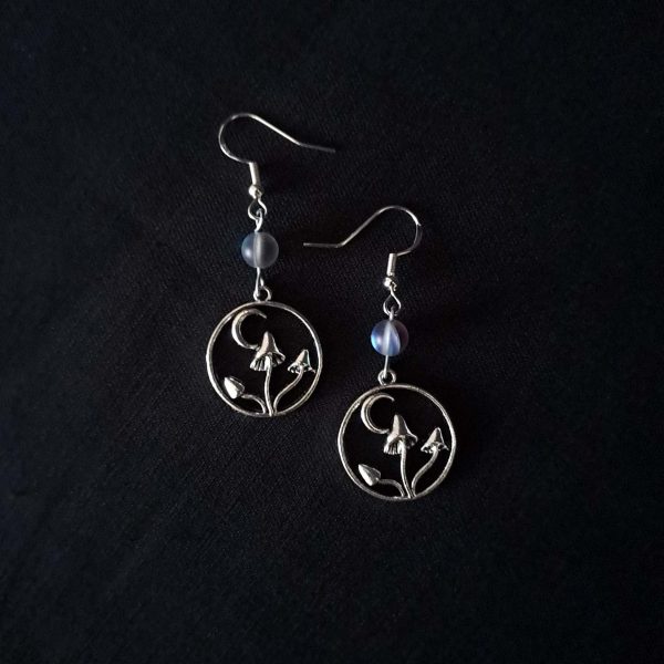Nocturnal mushroom earrings. A stainless steel charm contains three rising mushrooms, and a half moon. Above the charms lays a translucent iridescent grey-blue bead, reminiscent of moonstone. Very witchy and gothic vibes