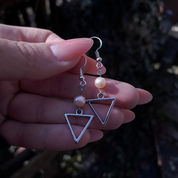 A pair of dangle earrings featuring silver triangle frames suspended from irregular peachy pearls.
