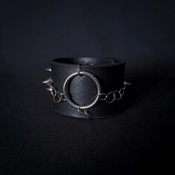 Black leather wristband with stainless steel spikes in assymetrical placement. Intertwined rings forming a chain and connecting th center large steel o-ring. A unique twist to a classis alternative fashion accessory of gothic or punk styles.