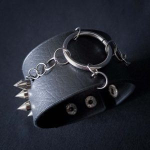 Black leather wristband with stainless steel spikes in assymetrical placement. Intertwined rings forming a chain and connecting th center large steel o-ring. A unique twist to a classis alternative fashion accessory of gothic or punk styles.