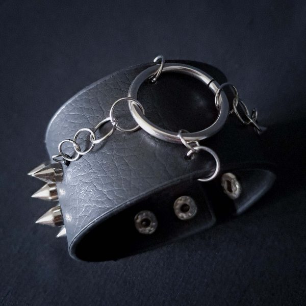 Black leather wristband with stainless steel spikes in assymetrical placement. Intertwined rings forming a chain and connecting th center large steel o-ring. A unique twist to a classis alternative fashion accessory of gothic or punk styles.