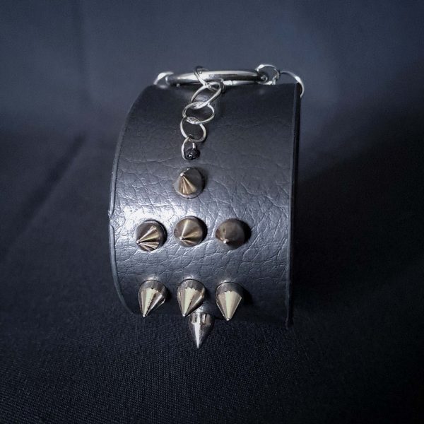 Black leather wristband with stainless steel spikes in assymetrical placement. Intertwined rings forming a chain and connecting th center large steel o-ring. A unique twist to a classis alternative fashion accessory of gothic or punk styles.