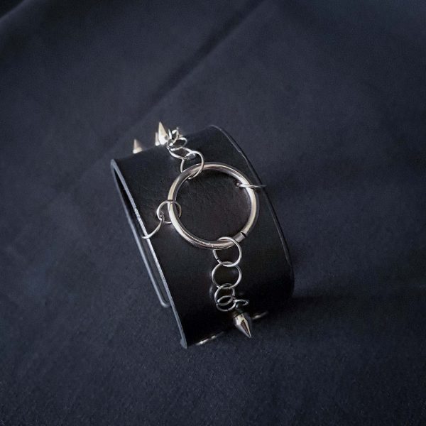 Black leather wristband with stainless steel spikes in assymetrical placement. Intertwined rings forming a chain and connecting th center large steel o-ring. A unique twist to a classis alternative fashion accessory of gothic or punk styles.