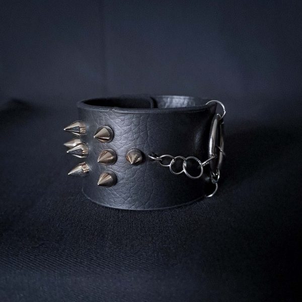 Black leather wristband with stainless steel spikes in assymetrical placement. Intertwined rings forming a chain and connecting th center large steel o-ring. A unique twist to a classis alternative fashion accessory of gothic or punk styles.
