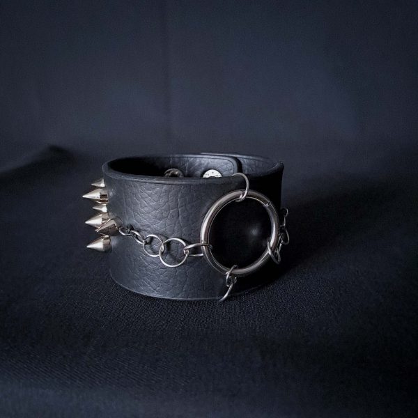 Black leather wristband with stainless steel spikes in assymetrical placement. Intertwined rings forming a chain and connecting th center large steel o-ring. A unique twist to a classis alternative fashion accessory of gothic or punk styles.