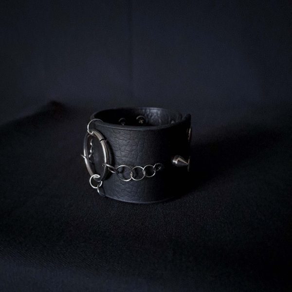 Black leather wristband with stainless steel spikes in assymetrical placement. Intertwined rings forming a chain and connecting th center large steel o-ring. A unique twist to a classis alternative fashion accessory of gothic or punk styles.
